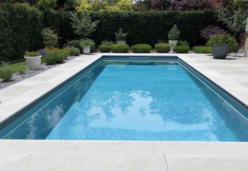 a small rectangular inground pool with green plants in the background